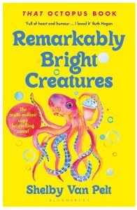 The front cover of the book Remarkably Bright Creatures by Shelby Van Pelt. The cover is a bright yellow background with blue text giving the title and author's name. There is an illustration of a pink and blue octopus surrounded by bubbles. The octopus' body is largely pink with blue suckers on his tentacles. He is surrounded by bubbles, and is holding what looks like a take away cup with something like a milkshake in it.