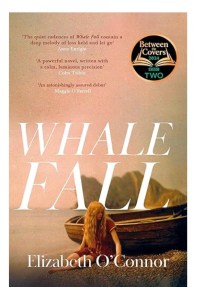 The front cover of the book Whale Fall by Elizabeth. The title and author name appear in white writing on a dusky pink background. A girl is sat on a shingle beach against a wooden sailing boat. She has long, wavy blonde hair and is wearing matching dark red with white piping top and shorts.